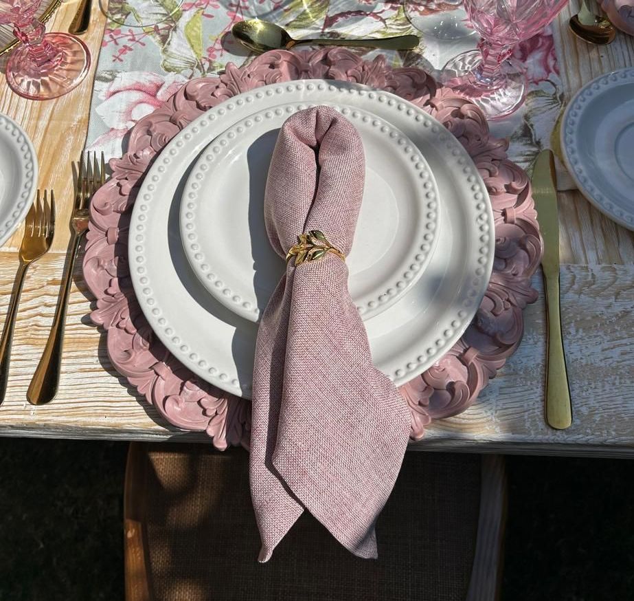 Decoración de mesa con detalles en rosa: base, platos, servilleta con aro, cubiertos dorados.