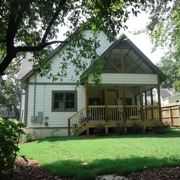 White house with wooden porch and green lawn, trees in yard.