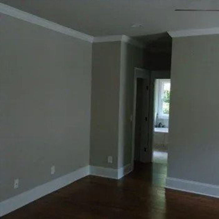 Empty room with gray walls, white trim, and dark wood floors; door leads to a bathroom.