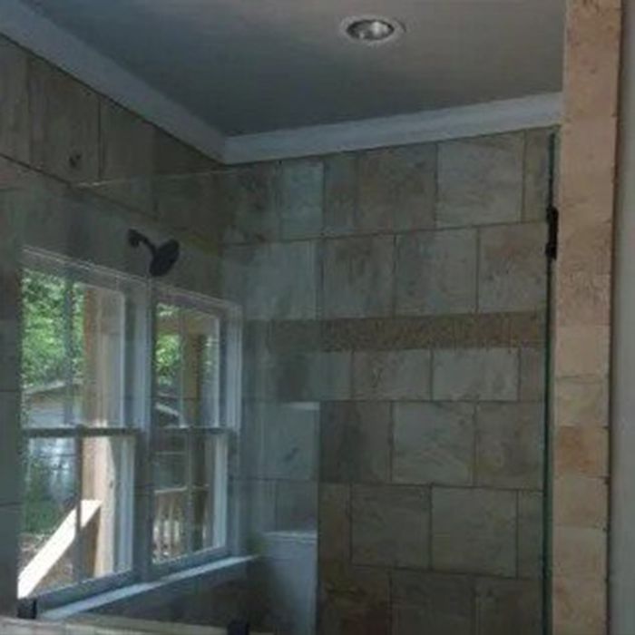 Bathroom with a glass shower door and window, featuring tan tile walls and white trim.