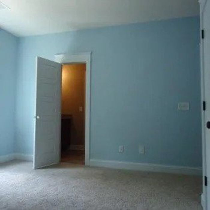 Empty room with light blue walls, white door, doorway to a room with a brown interior, and light-colored carpet.