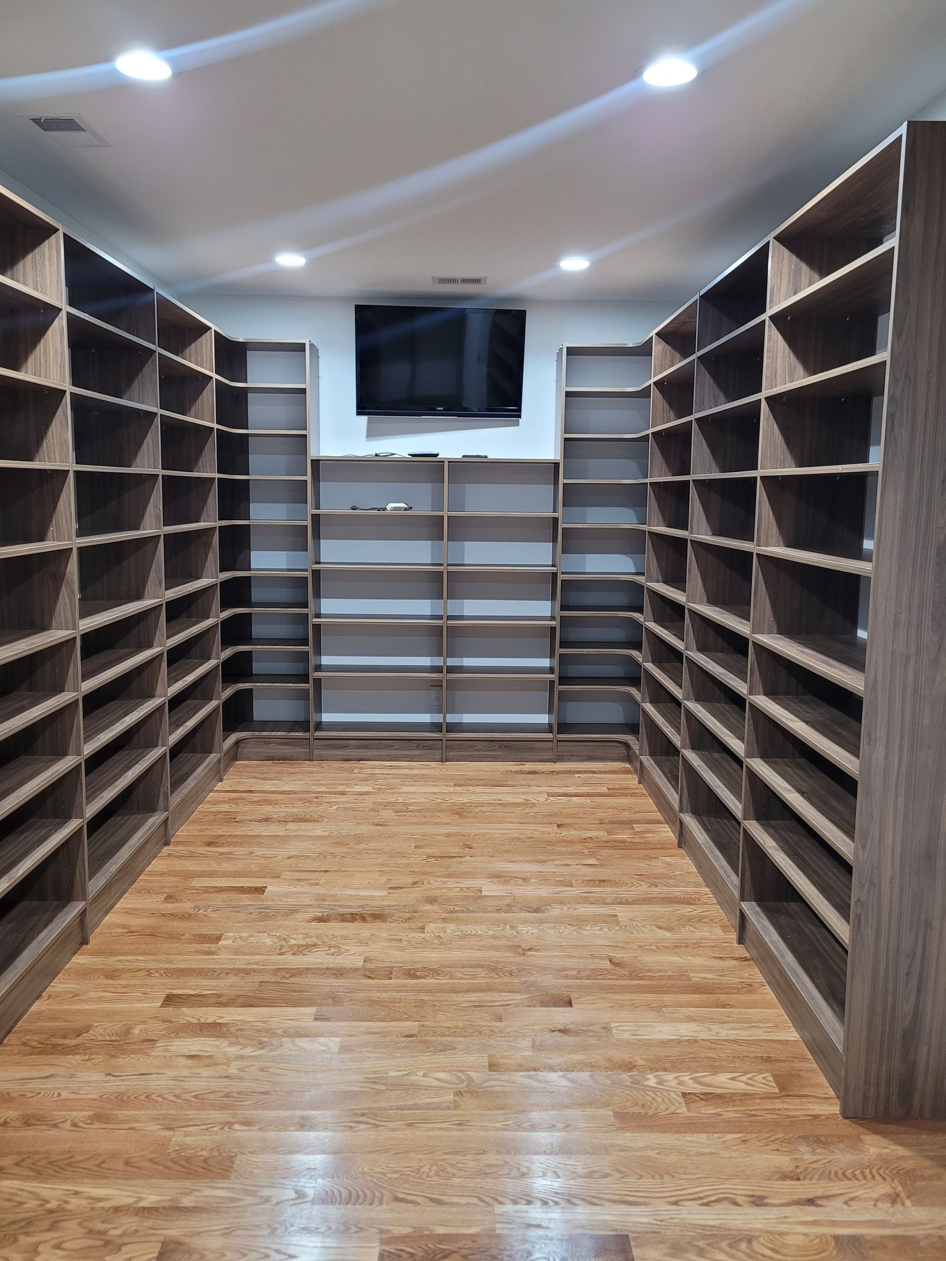 Walk-in closet with rows of shelves on both sides, wood floor, TV centered on the back wall.