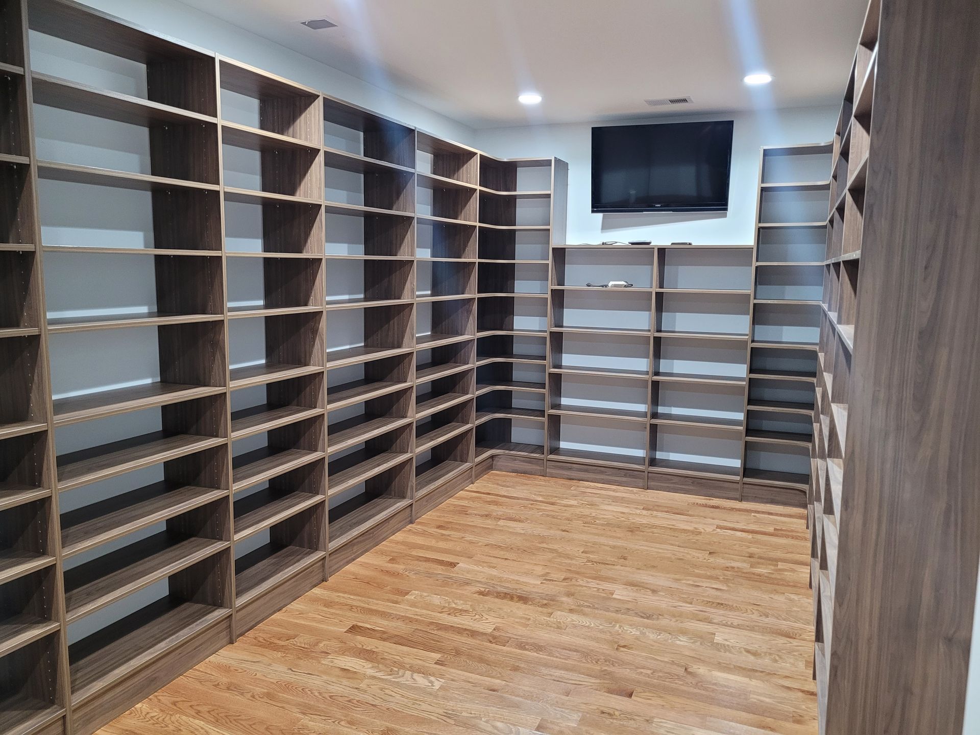 Built-in dark brown wooden bookshelves line the walls of a room with hardwood floors; a TV is mounted above some shelves.