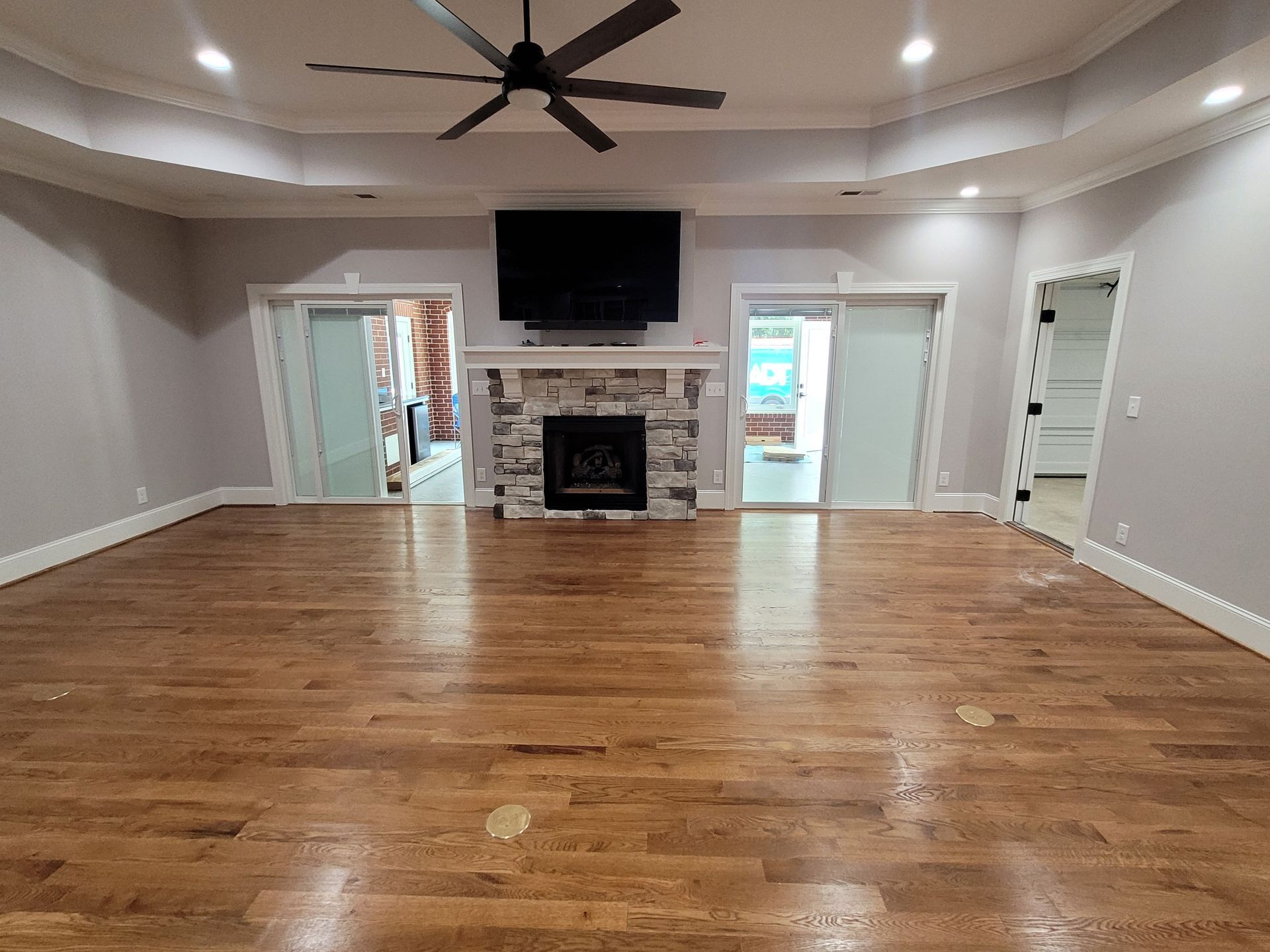 Spacious room with hardwood floors, fireplace, TV, and sliding doors; ceiling fan, neutral walls.