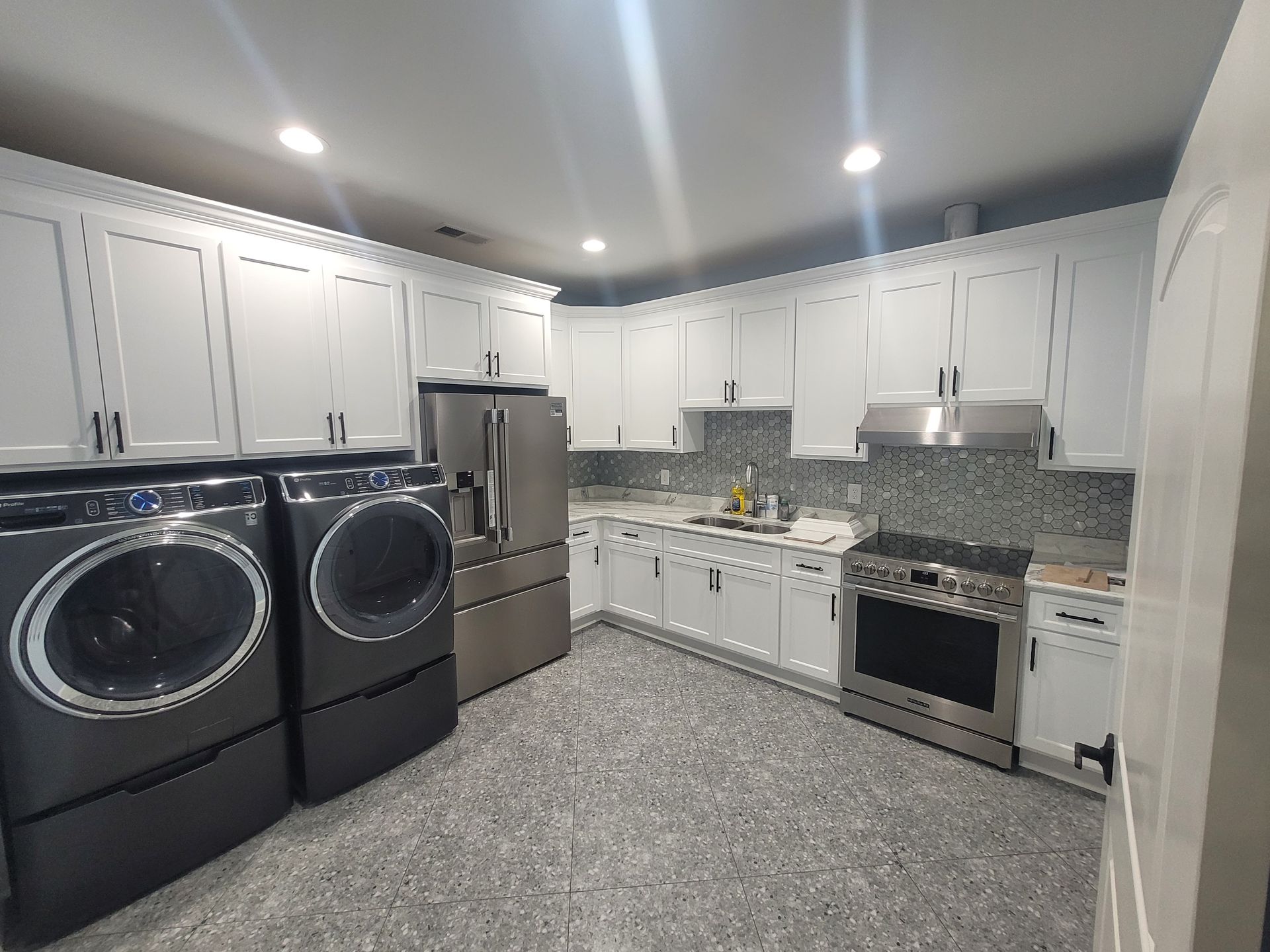 Laundry appliances and stainless steel kitchen appliances in a gray-floored room with white cabinets.
