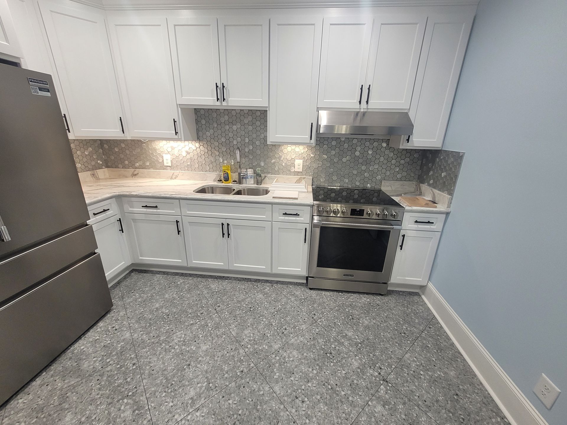 White kitchen with stainless steel appliances and gray speckled flooring.