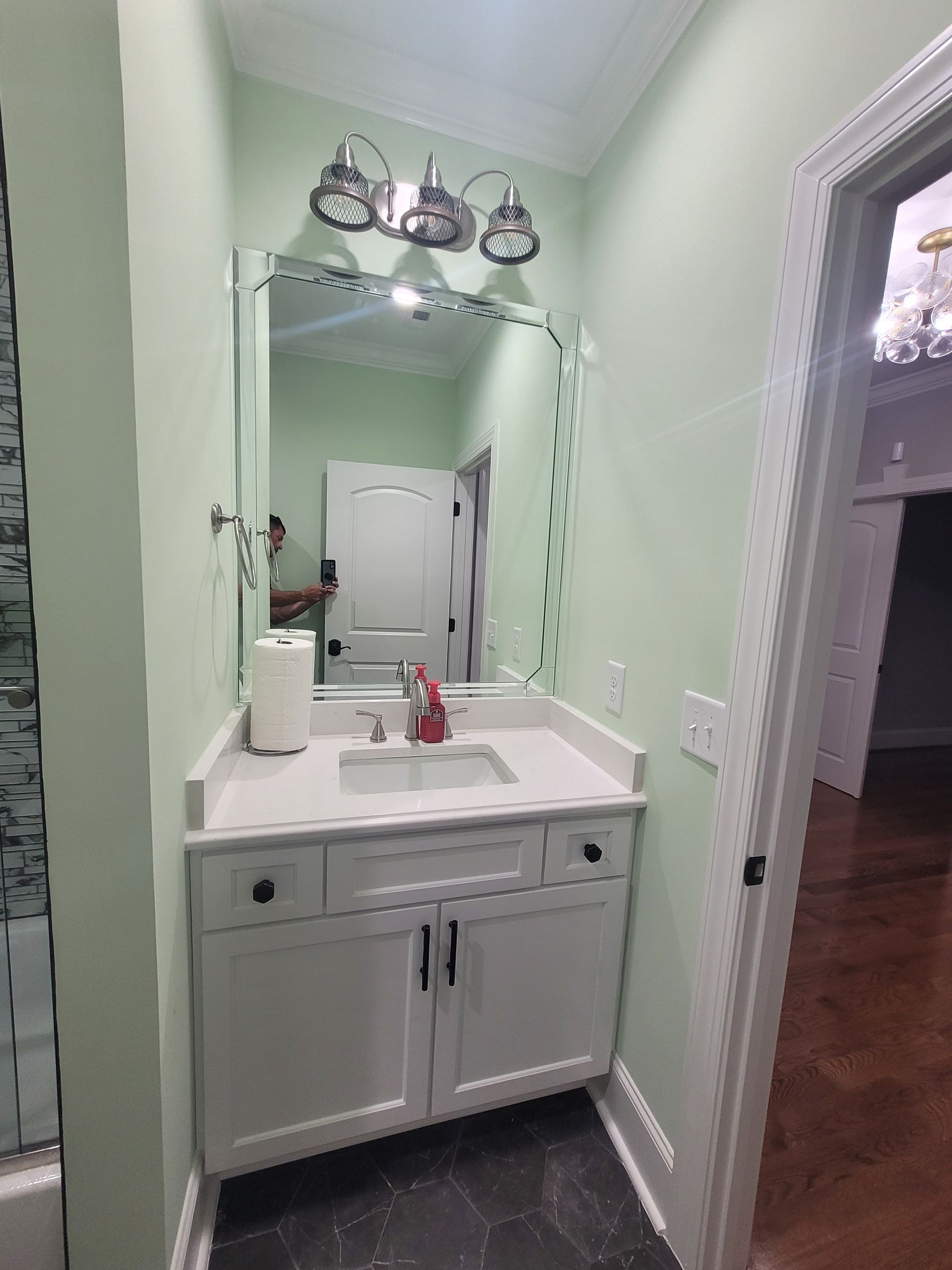 White bathroom vanity with mirror, lights, and open door. Green walls.