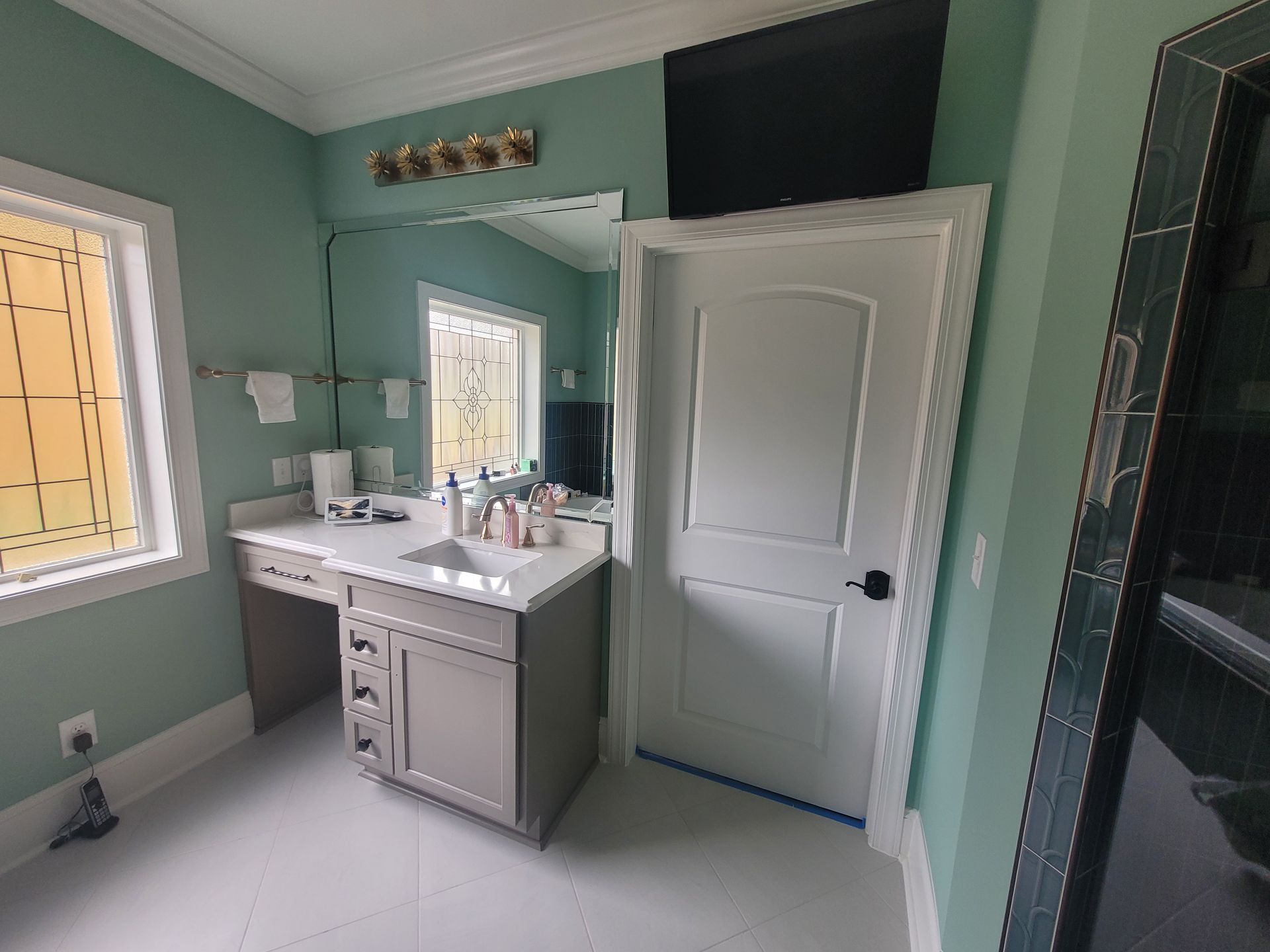 Bathroom with a vanity, window, and white door; pale green walls and white floor.