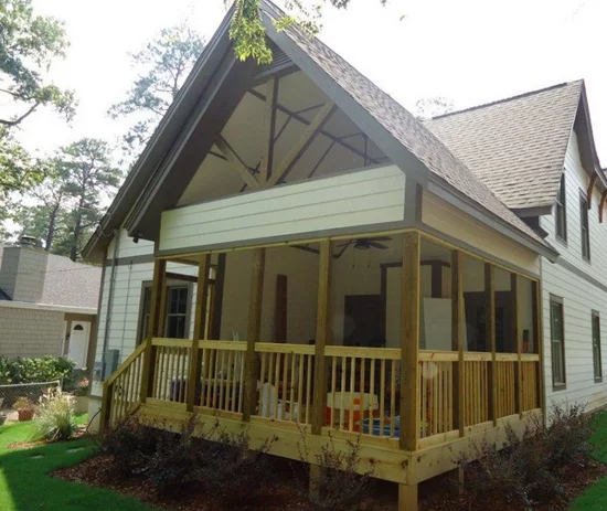 Wooden-railed porch of a two-story house with light siding and brown roof.