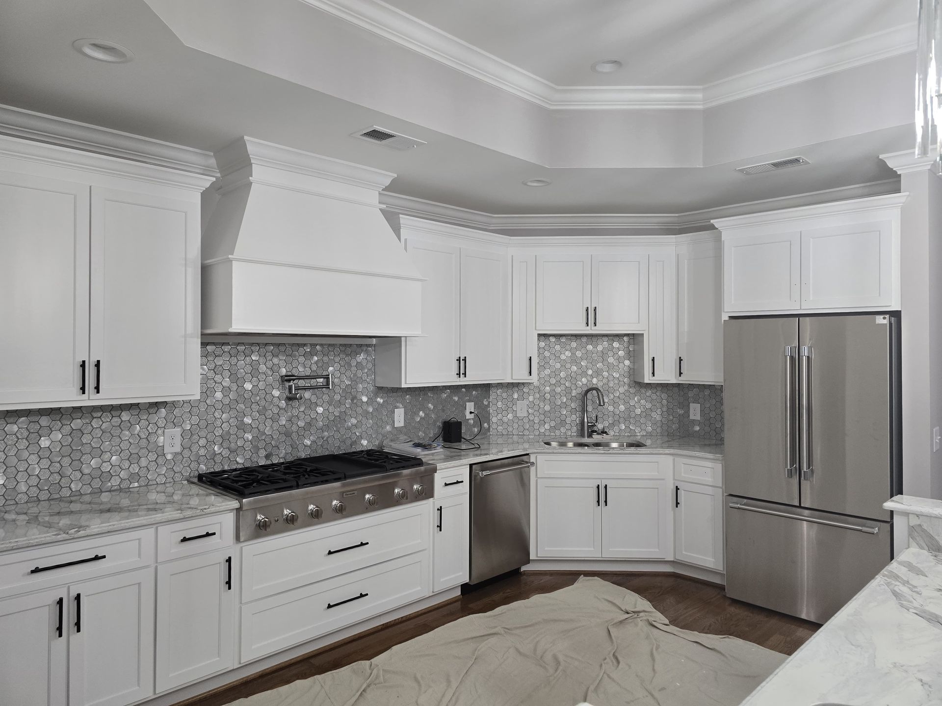 White kitchen with stainless steel appliances, gray backsplash, and dark hardware.