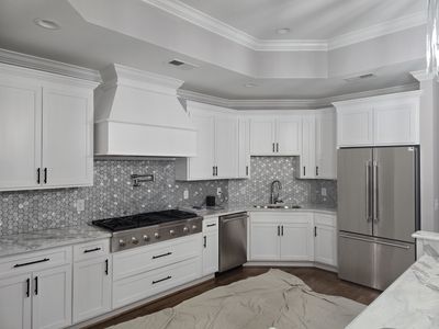 White kitchen with stainless steel appliances, gray backsplash, and dark hardware.