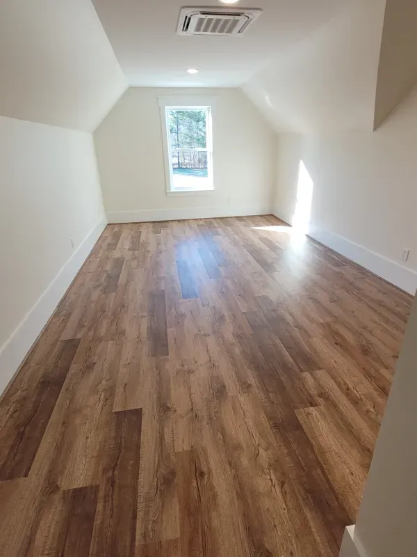 Attic room with wood-look flooring, sloped ceiling, and a small window. Natural light fills the space.
