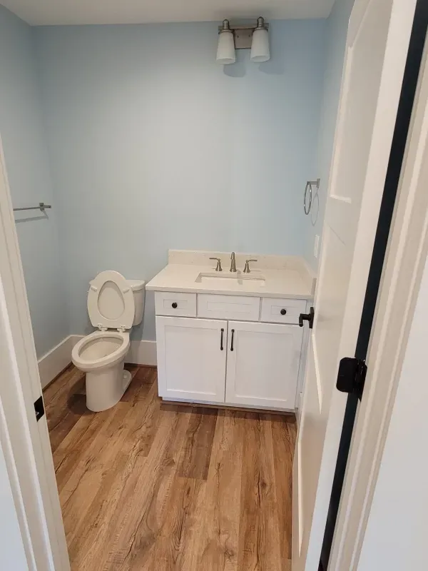 Small bathroom with white vanity, toilet, and light blue walls, seen from the doorway.