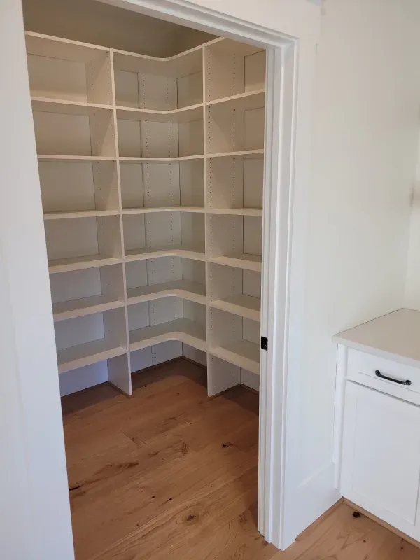 A walk-in pantry with white shelves, hardwood floor, and a countertop.