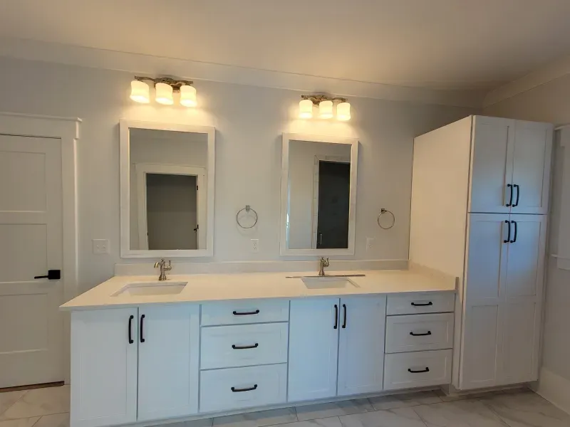 White bathroom with double sinks, mirrors, cabinets, and gold light fixtures.