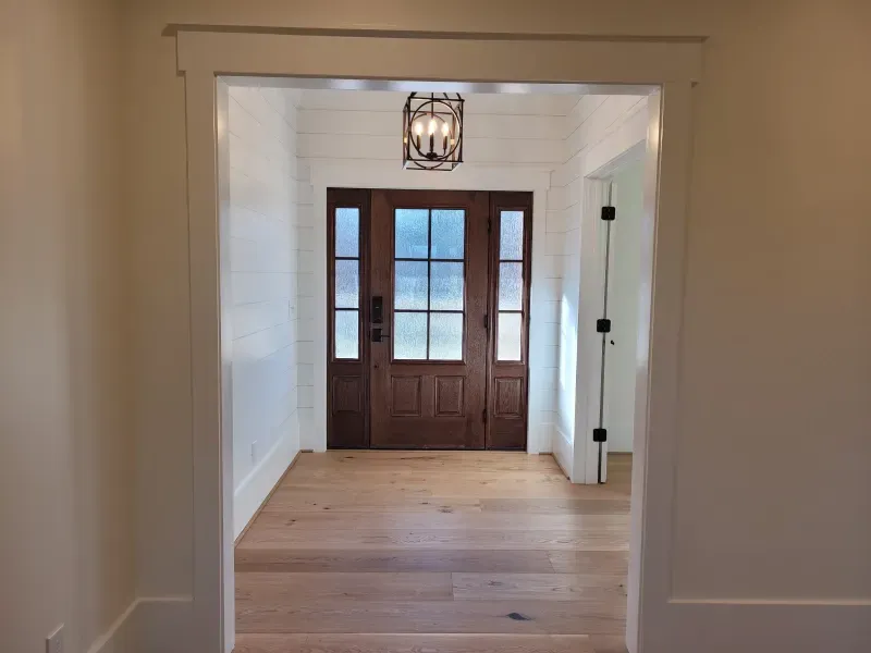 Wooden front door framed by white walls and trim; hardwood floors.