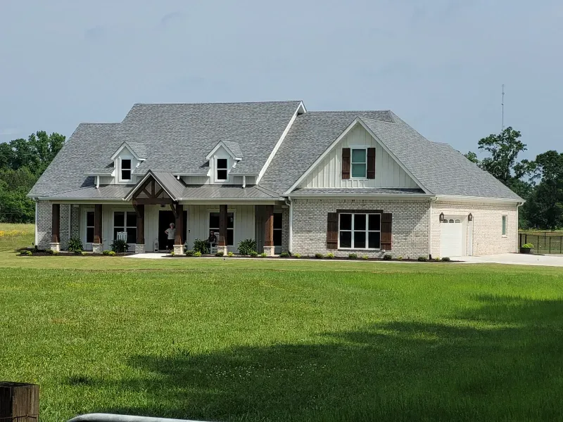 Large, light brick house with gray roof, white trim, brown shutters and a green lawn.