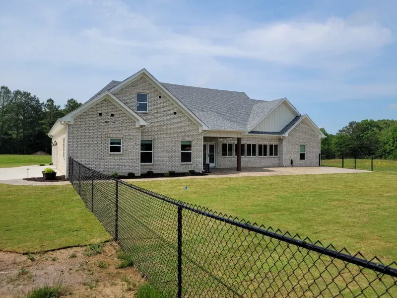 Brick house with a gray roof, black fence, and green lawn under a blue sky.