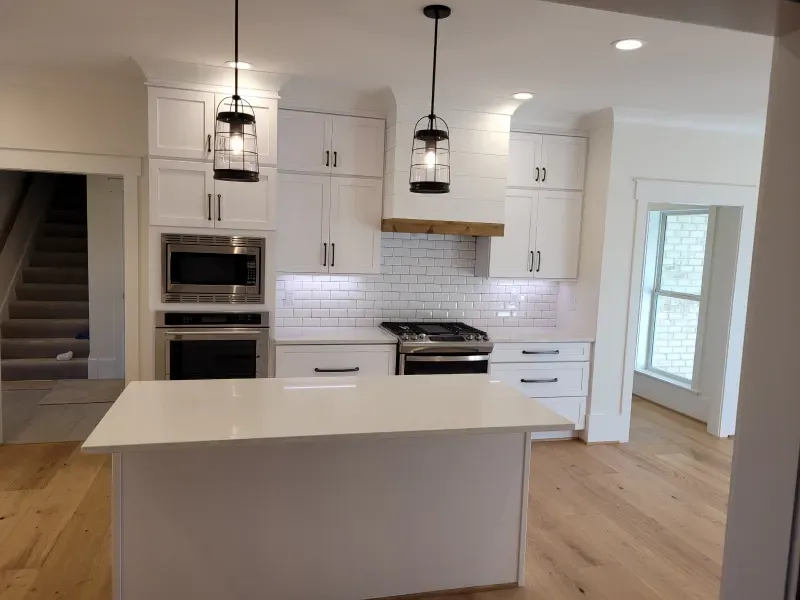 Modern white kitchen with island, stainless steel appliances, and wood floors.