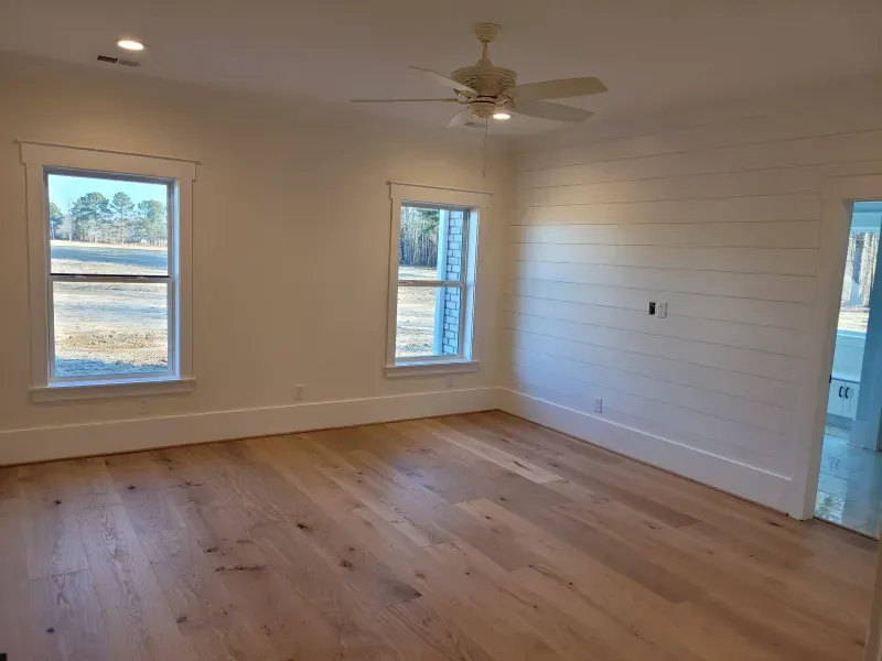 Spacious room with hardwood floors, two windows, shiplap wall, and ceiling fan.
