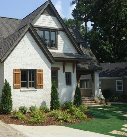 Cottage-style home with white stucco exterior, brown shutters and trim, small front yard with landscaping.