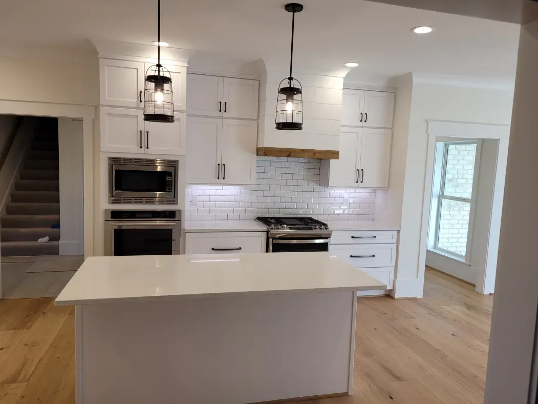 Bright white kitchen with island, stainless steel appliances, wood accents, and pendant lights.