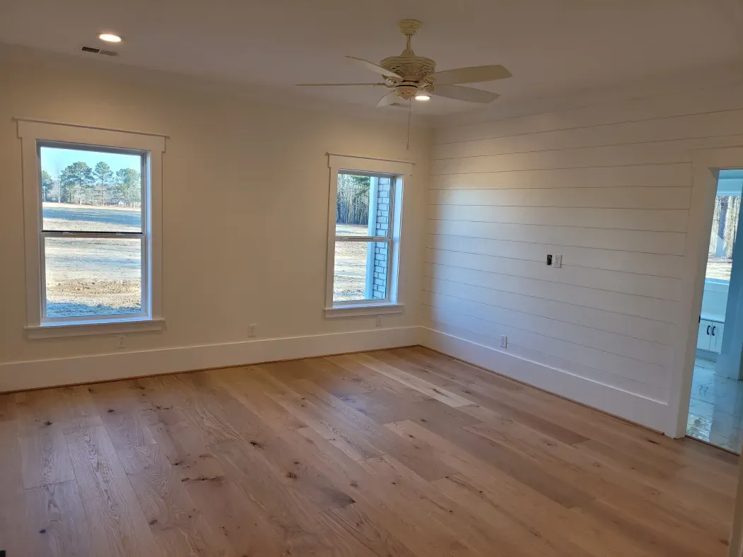 Empty bedroom with wood floor, two windows, and shiplap accent wall.