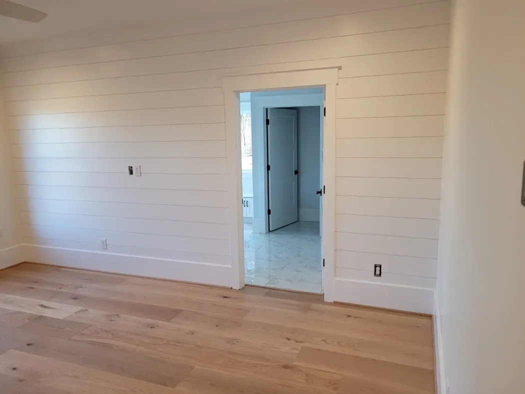 Empty bedroom with white shiplap walls, wood floor, and a doorway.