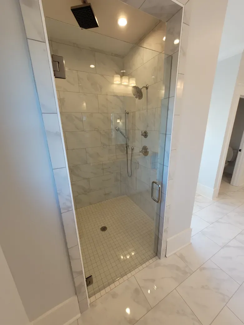 Glass shower with white marble tile, chrome fixtures, in a bright, modern bathroom.