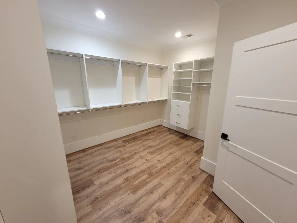 Walk-in closet with white shelving, a hanging rod, and wood-look flooring; white door on the right.