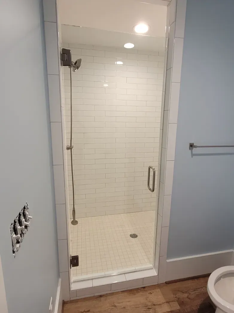 Bathroom with glass shower door, white tile, and light blue walls.