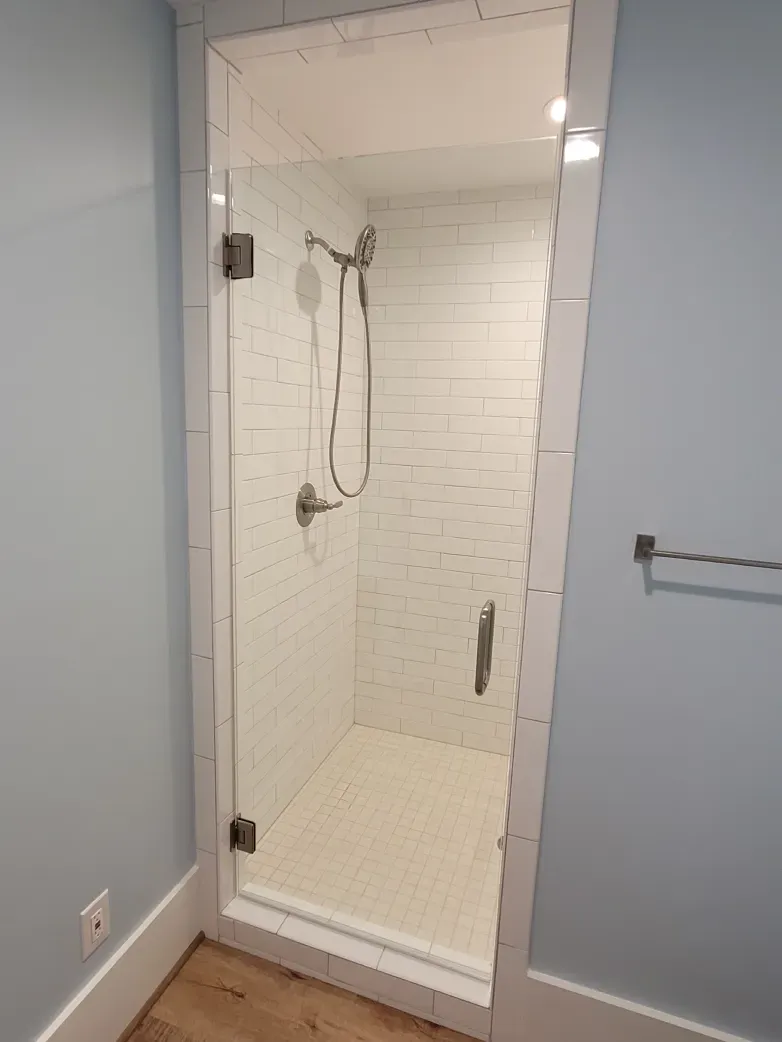 Glass shower enclosure in a bathroom with white tile and light blue walls.