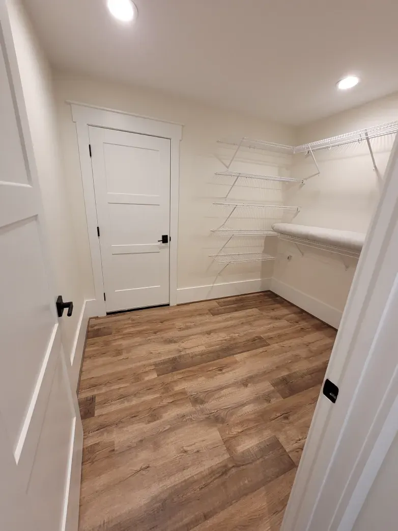 Small closet with wood-look floor, white walls, door, shelves, and overhead lighting.