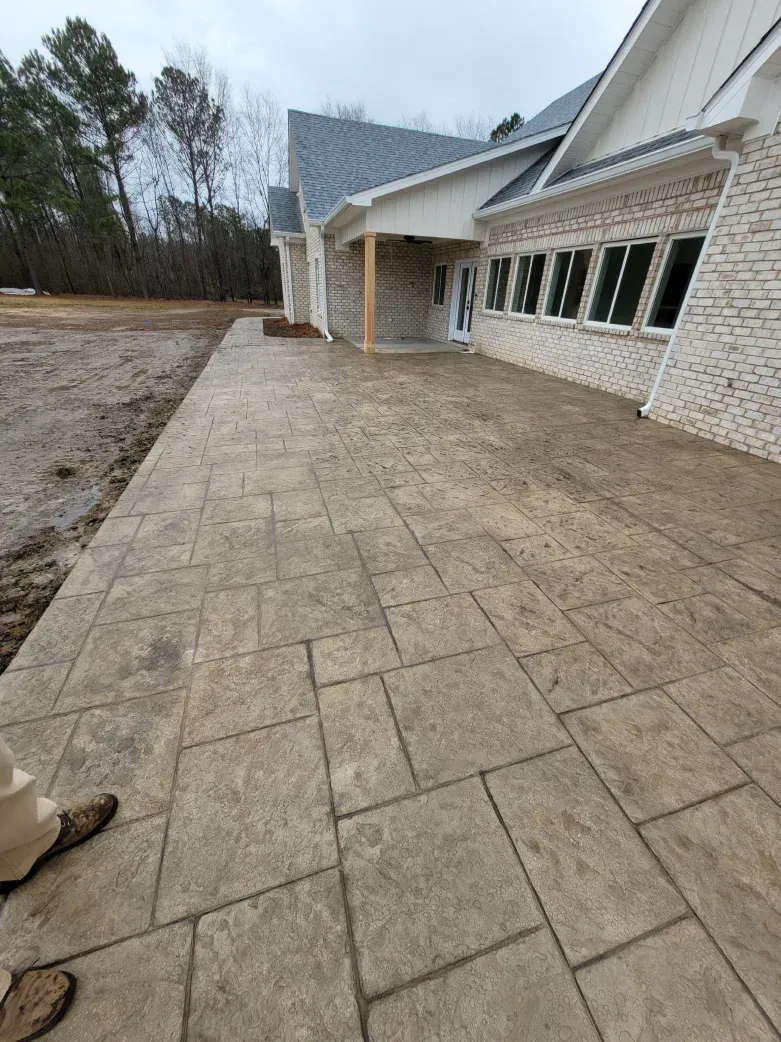 Stamped concrete walkway leads to a building with stone and white siding. Cloudy day.