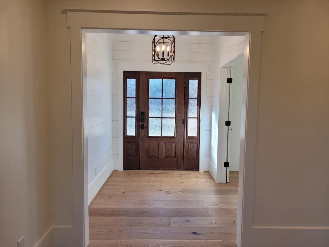 Wooden doorway leading to a front door with sidelights and a hanging lantern. Light wood floors.