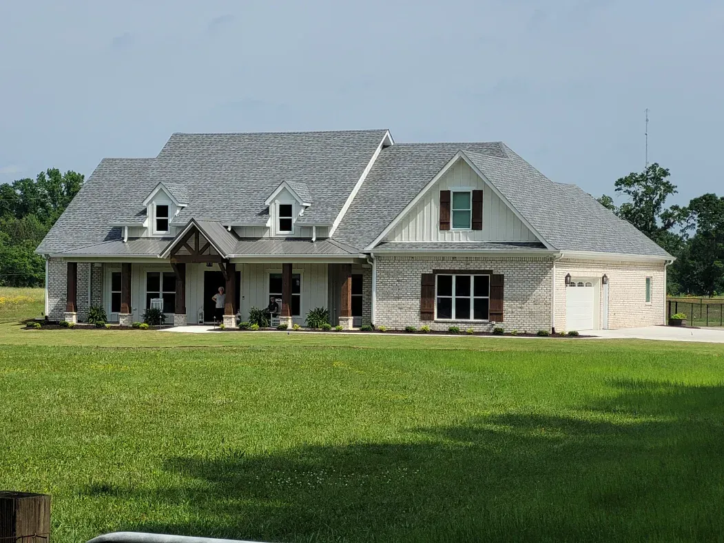 A light brick and white home with a gray roof in a grassy field.