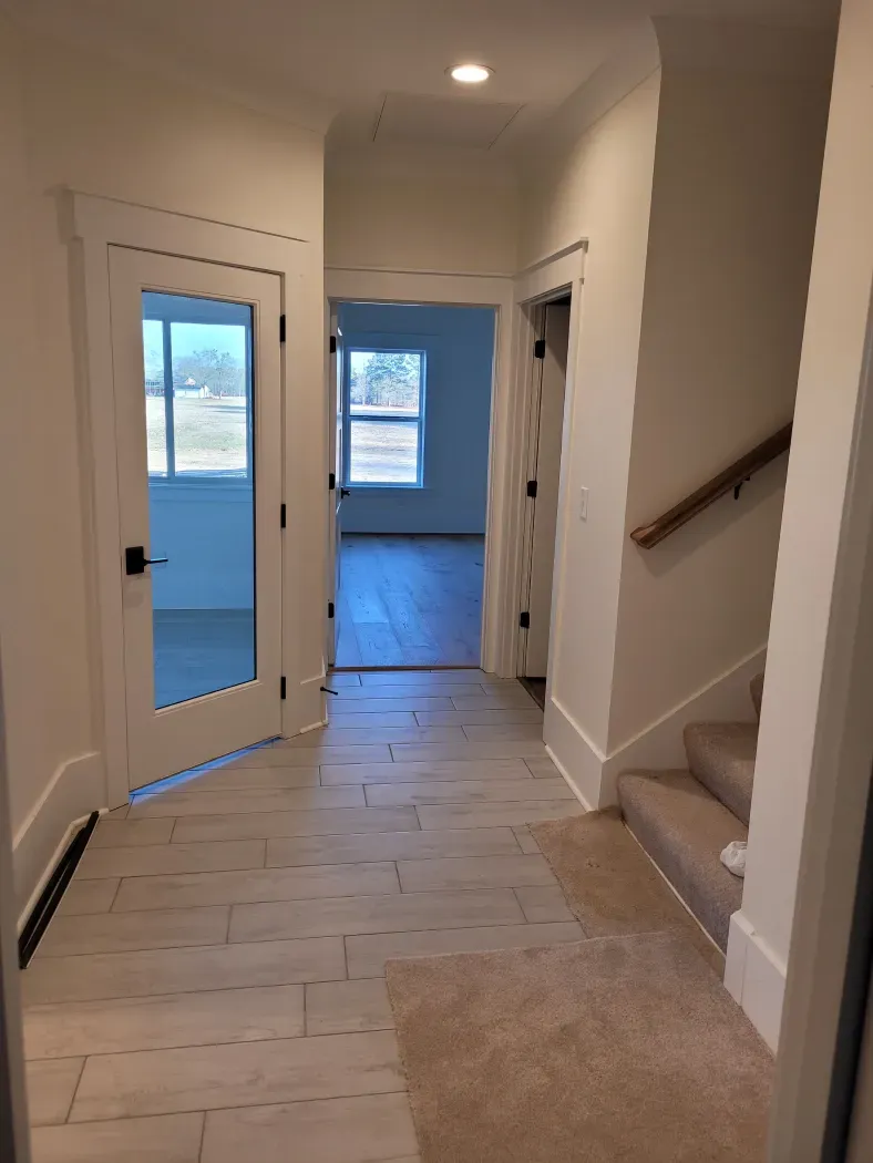 Hallway with light wood floors, white walls, glass door, and stairs with a carpet runner.