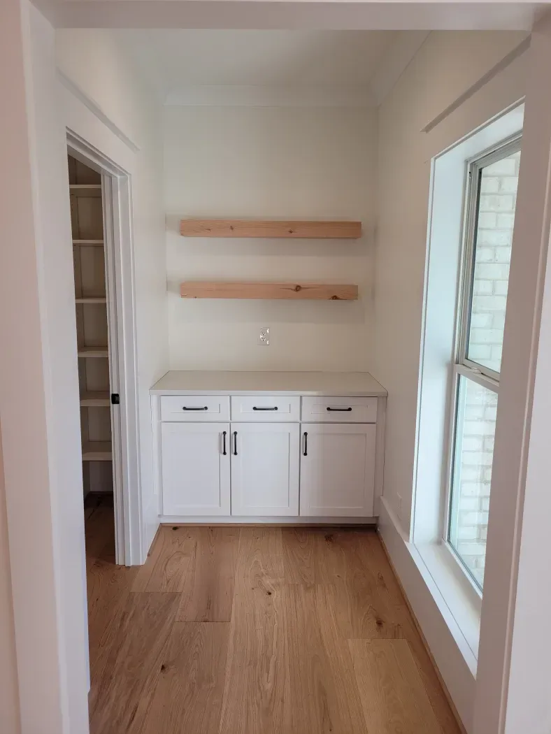 White built-in cabinets with floating shelves in a room with wood floors and a window.