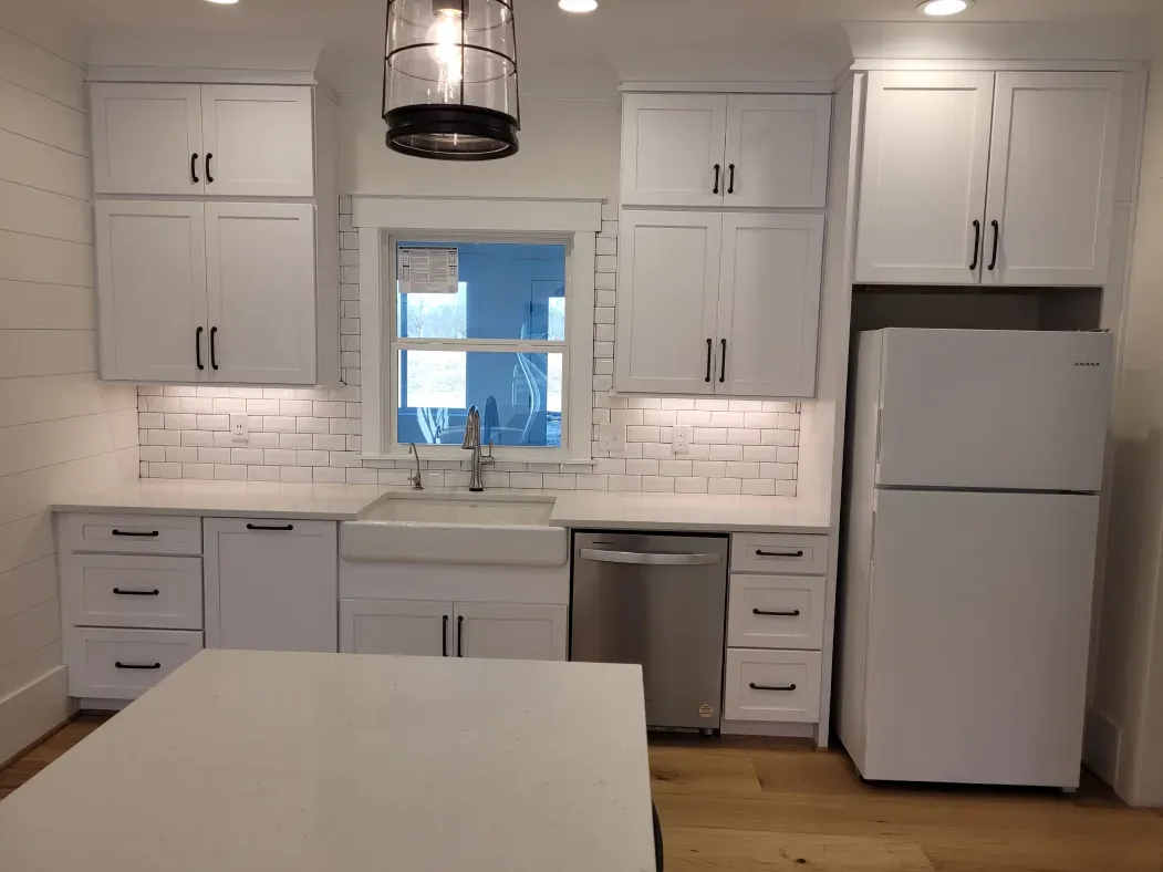 White kitchen with white cabinets, brick backsplash, and a window above the sink.