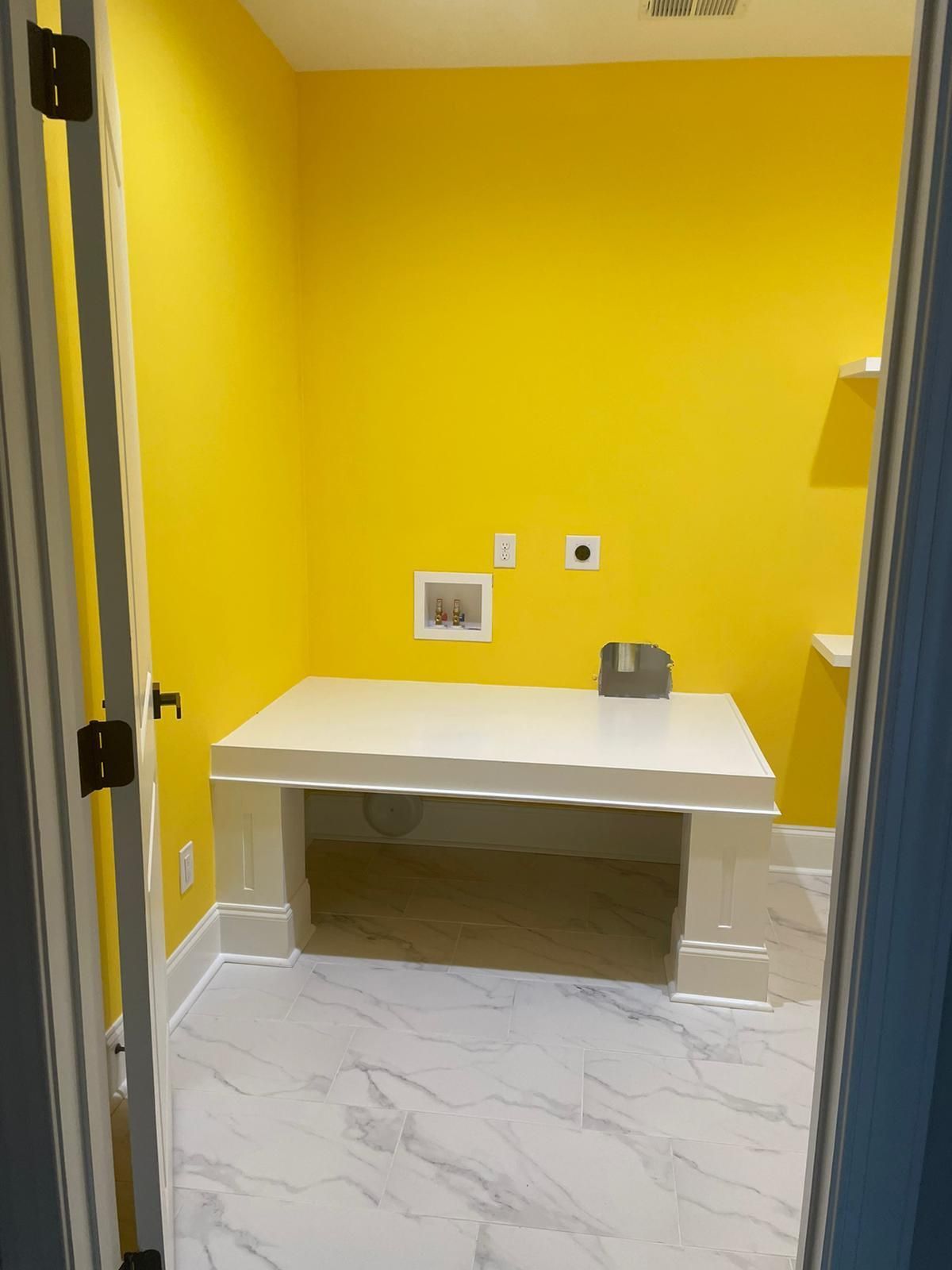 Yellow-walled laundry room with a white countertop and marble-look floor, viewed from the doorway.