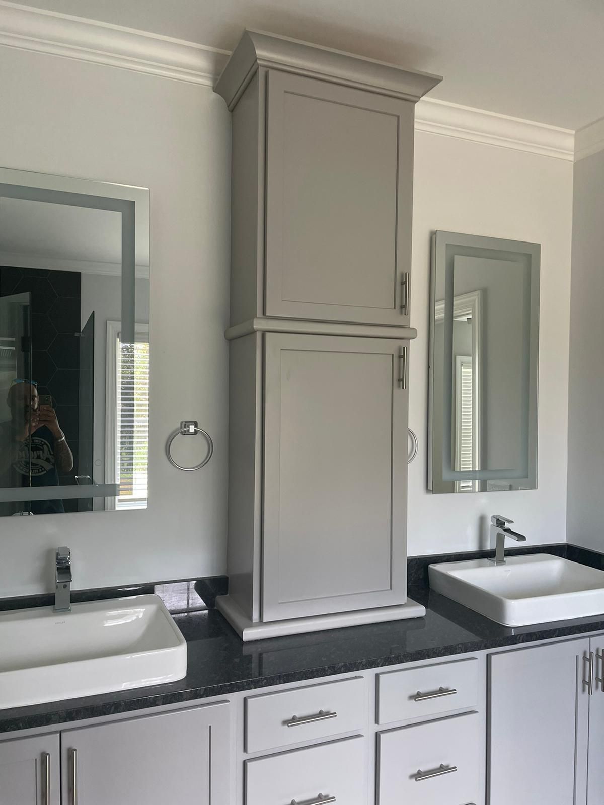 Gray bathroom with a tall cabinet, two sinks, and mirrors.