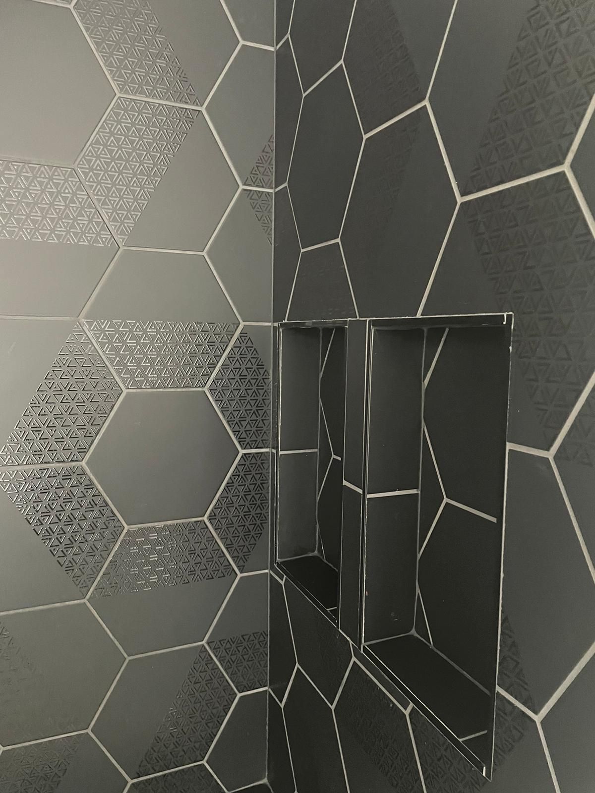 Dark gray tiled shower with geometric pattern and built-in shelves.