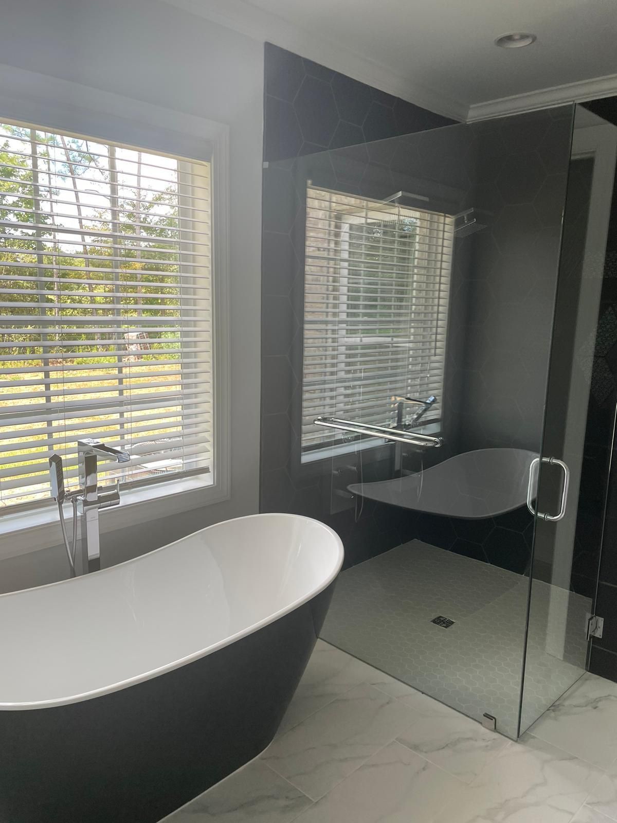 Bathroom with black soaking tub, glass shower, and window with blinds.