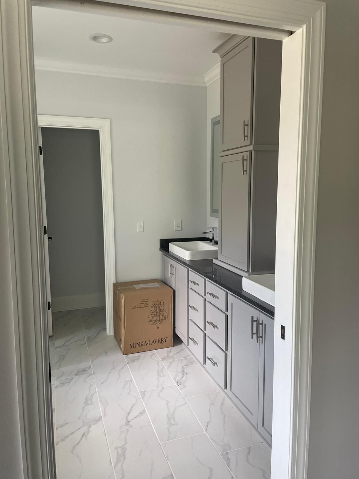 Bathroom with gray cabinets, black countertop, white sink, and tiled floor.