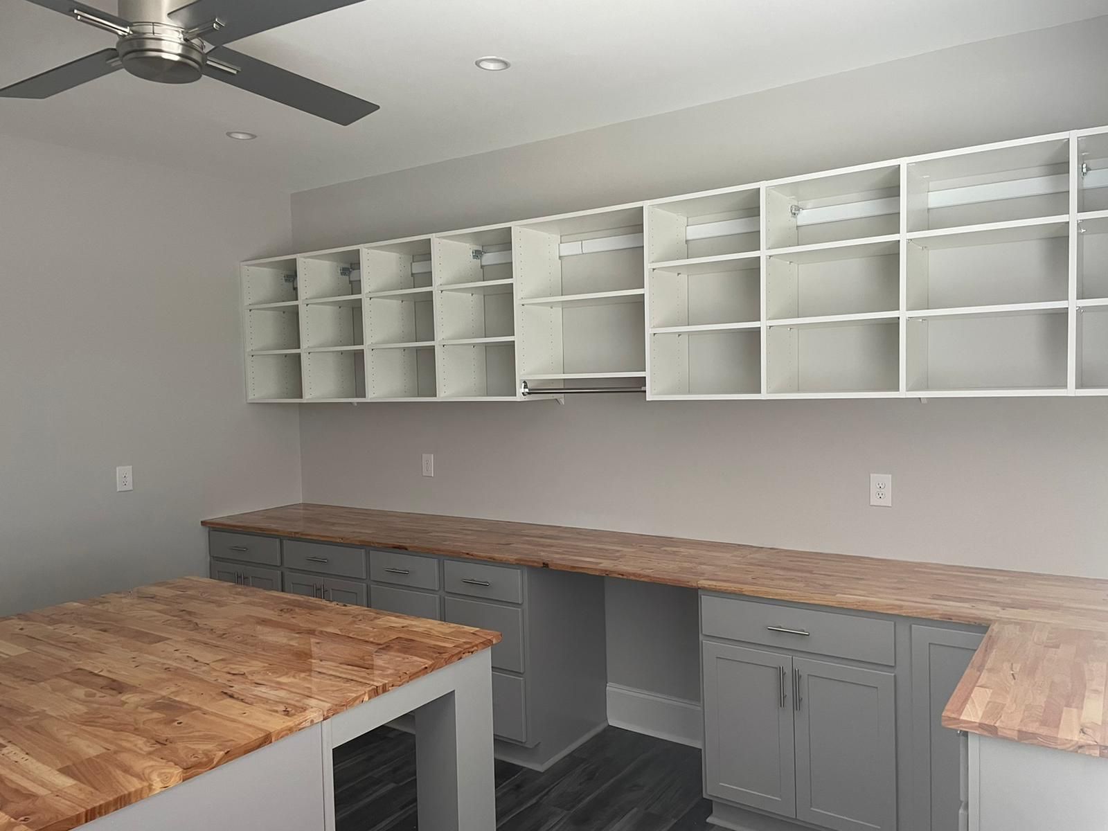 A room with a gray and wood cabinetry with white overhead shelves.