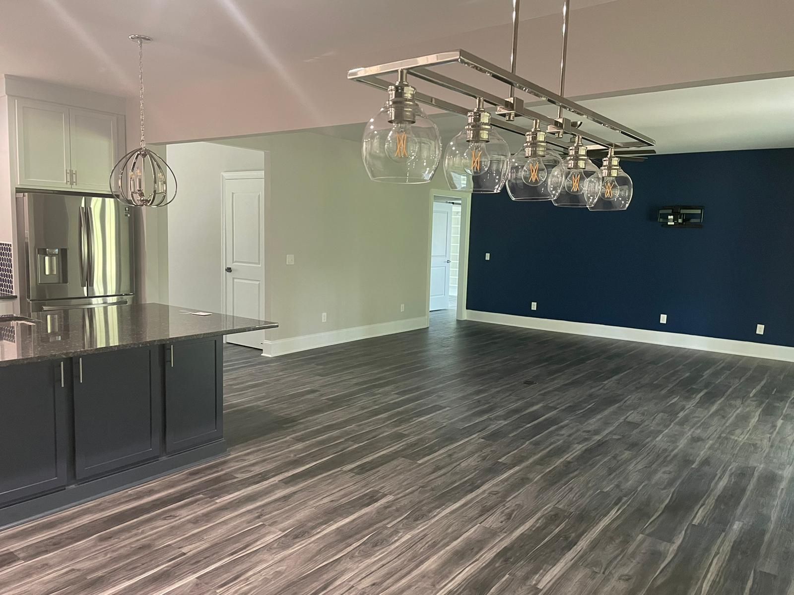 Modern open-concept kitchen and living area. Dark gray cabinets and flooring, navy accent wall, and pendant lighting.