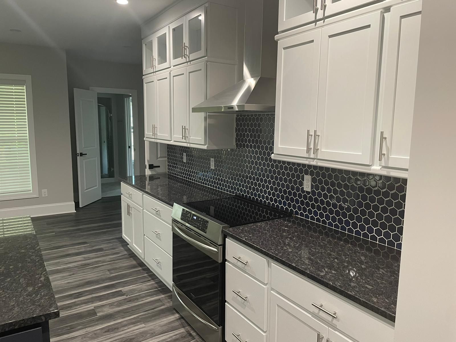 White kitchen with black countertops, backsplash, and cabinets. Stainless steel stove and vent hood.