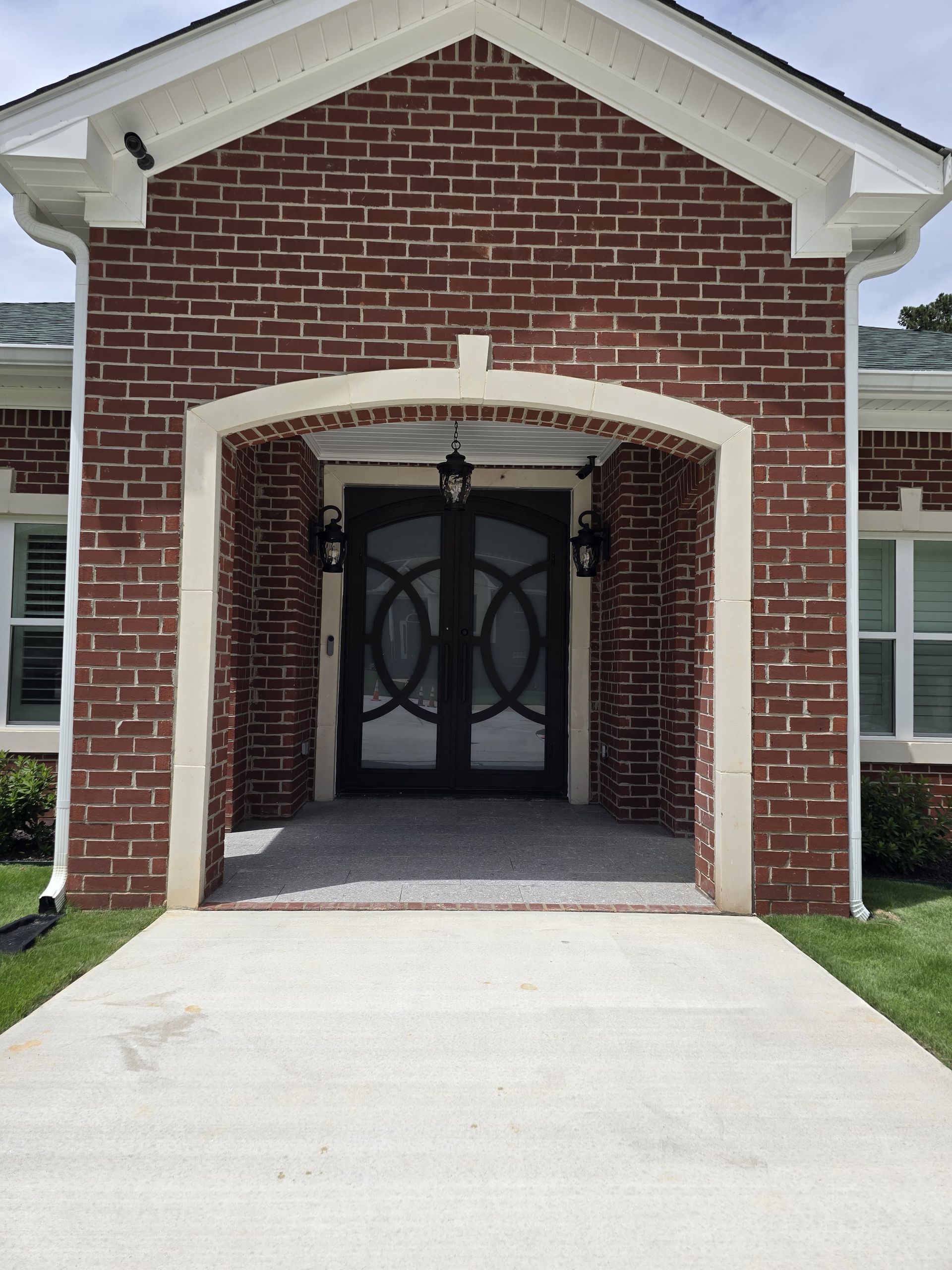 Red brick house entrance with arched doorway, black double doors, and concrete path.