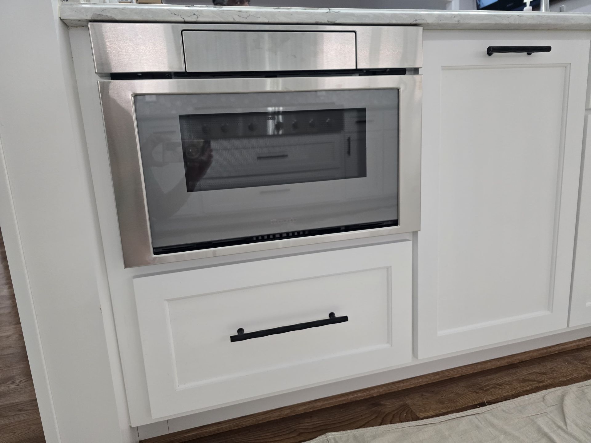 Built-in stainless steel microwave oven and white cabinetry with black hardware in a kitchen setting.