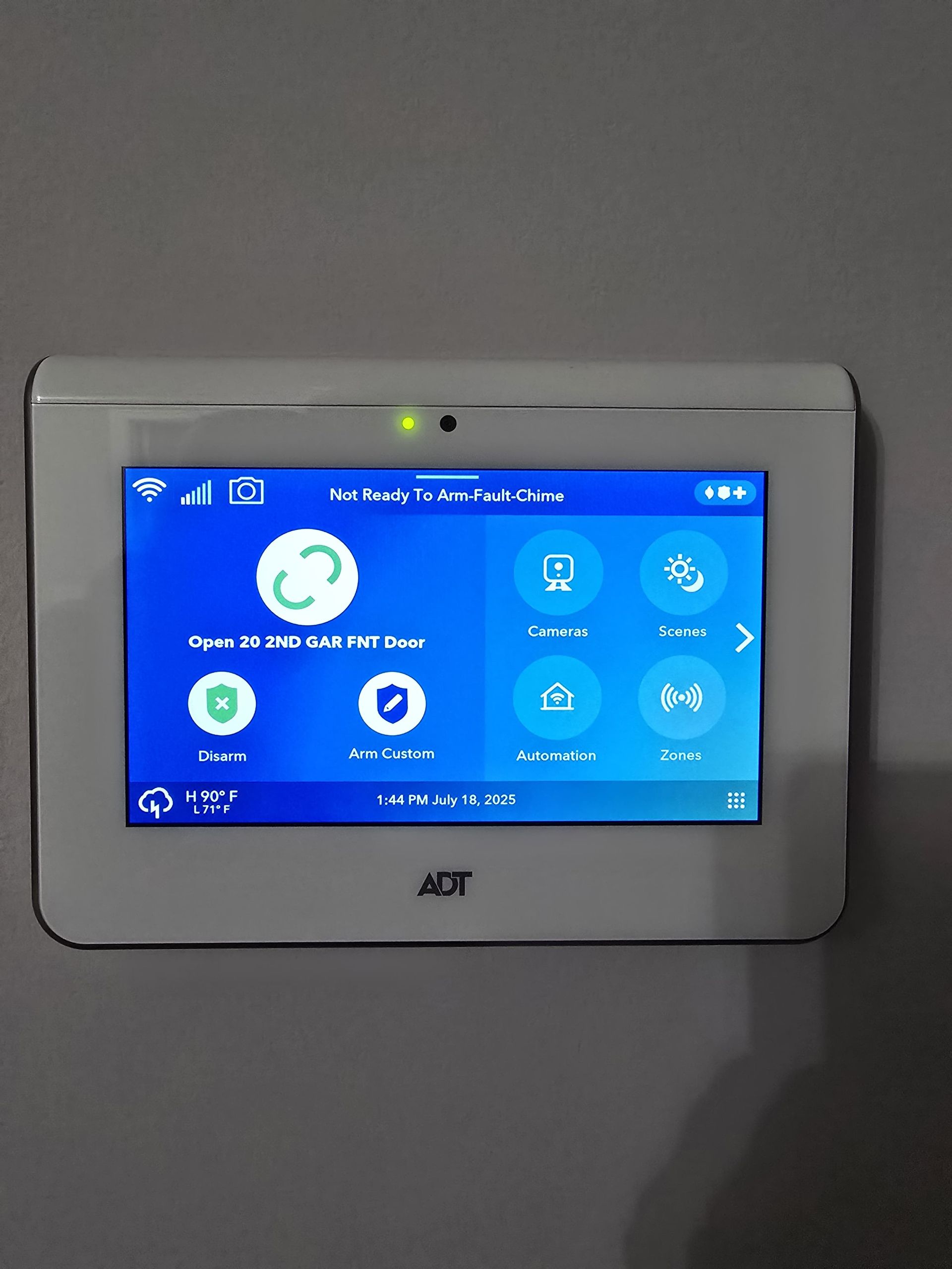 ADT security system control panel on a gray wall, blue screen with various icons.